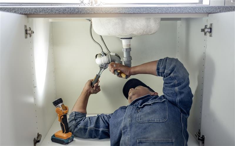 Plumber repairing pipes beneath a bathroom sink in Fountain