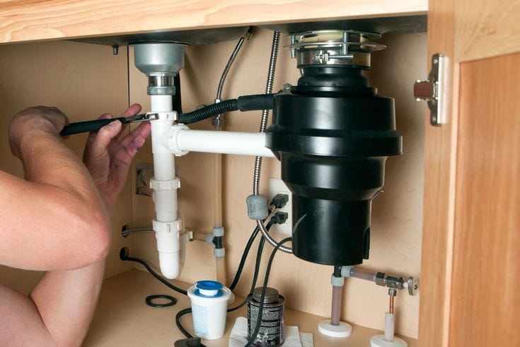 Plumber installing a garbage disposal beneath a kitchen sink in Fountain