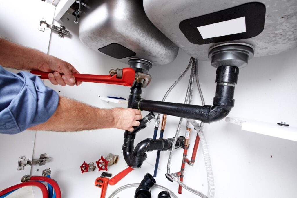 Plumber repairing drain pipes beneath a kitchen sink in Fountain